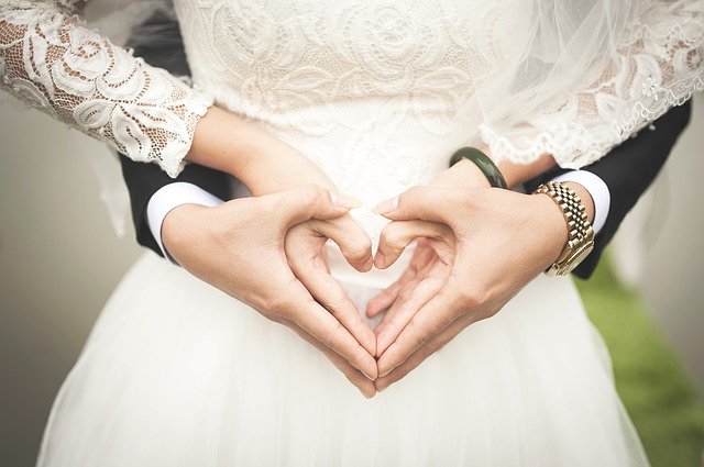 Svatební fotografie muž a žena s prsty do tvaru srdce.